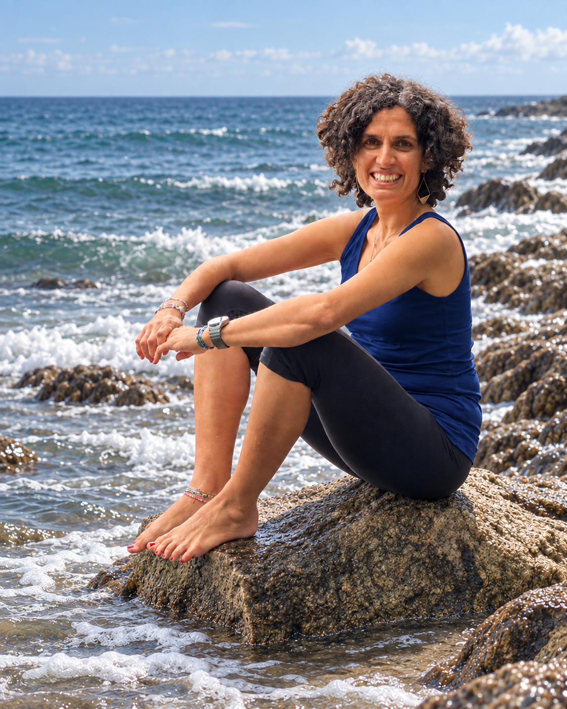 Kiran sitzt lächelnd auf einem Felsen am Meer